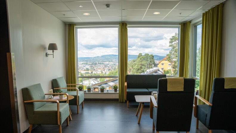 Et av stuerommene ved helsehuset. Stuen er innredet med en sofa og fire lenestoler. Fra stuen har man utsikt over hele Oslo by.