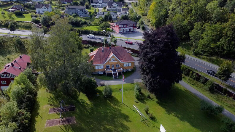 Luftfoto av en gul villa med stor hage på en solfylt dag.