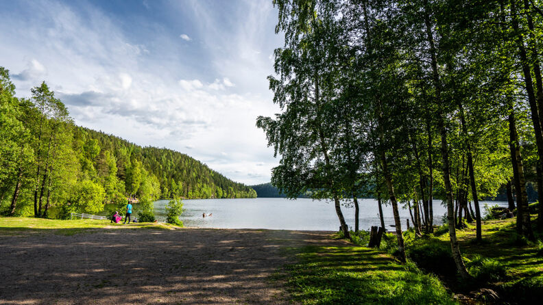 Lutvann i Østmarka med grusvei frem til badestedet. To personer bader i bakgrunnen.