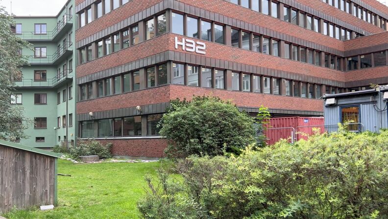 En brun mursteinsblokk med mange vinduer. På bygget står det H32. 