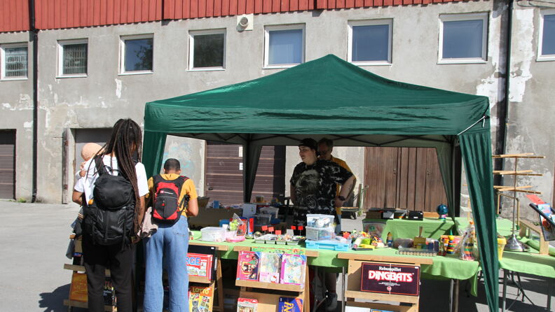 To mennesker som står foran en salgstelt med bøker og diverse produkter. Inne i salgsteltet står det også to mennesker.