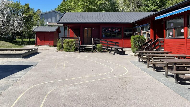 Barnehagens uteområde. Malt sykkelløpye på asfalt. Rødmalt barnehage i bakgrunnen.