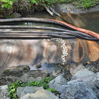 Oljeutslipp i en elv, med sorte og oransje ledninger som skiller forurenset vann fra rent vann