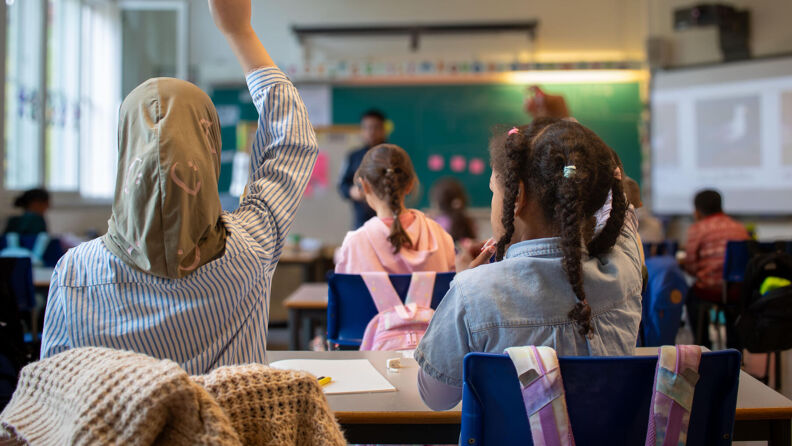 Barn som rekker opp hendene i et klasserom.