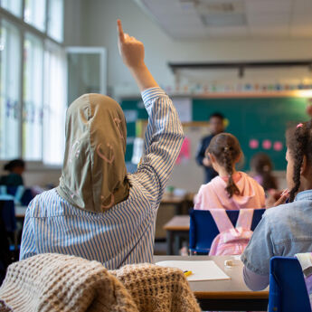 Barn som rekker opp hendene i et klasserom.