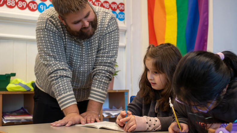 En lærer snakker til et barn som sitter på skolebenken.