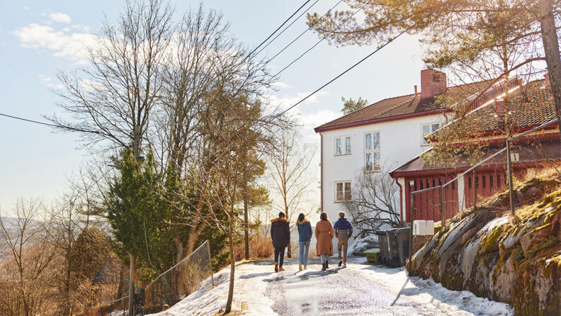 En gruppe på fire ungdommer går mot et hvitt hus på en topp om vinteren i solnedgang