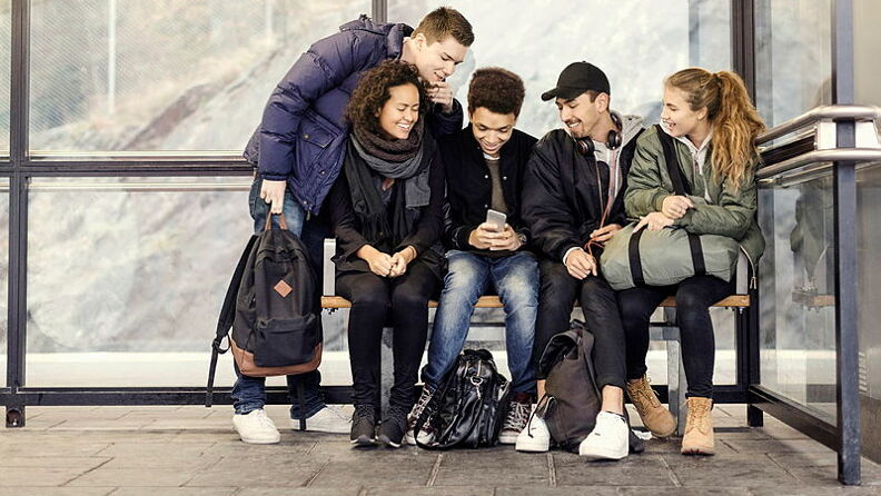  Gruppe med ungdommer sitter på en benk og ser i en telefon