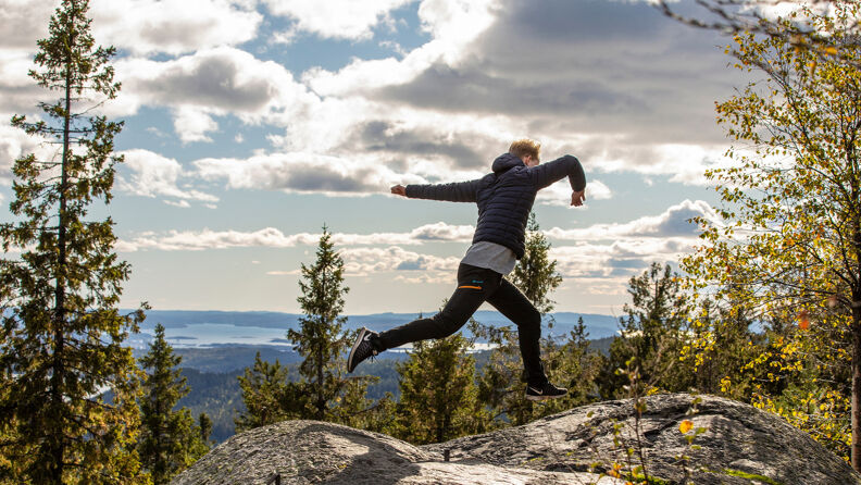 En mann hopper mellom to utsiktspunkter foran utsikten på Mellomkollen.