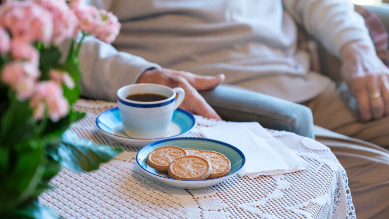 Eldre mann sitter ved bord med en kaffekopp og kjeks