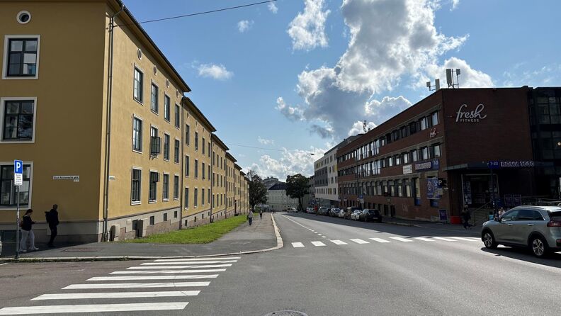 Fotografiet viser Sandakerveien sørover, fotgjengerfelt, fortau og veibane. Blå himmel.