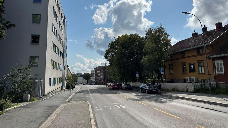 Fotografiet viser Sandakerveien med Lillo gård på høyre siden. Kjørebane og fortau. Blå himmel.