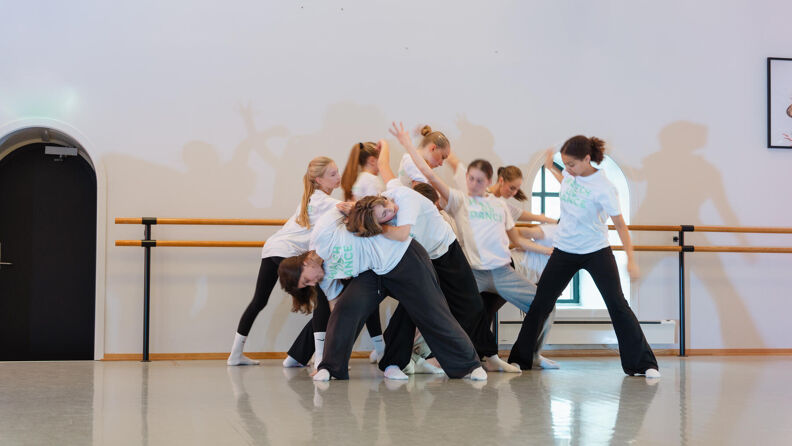 Gjeng med ungdommer danser i hvite skjorter og svarte bukser.