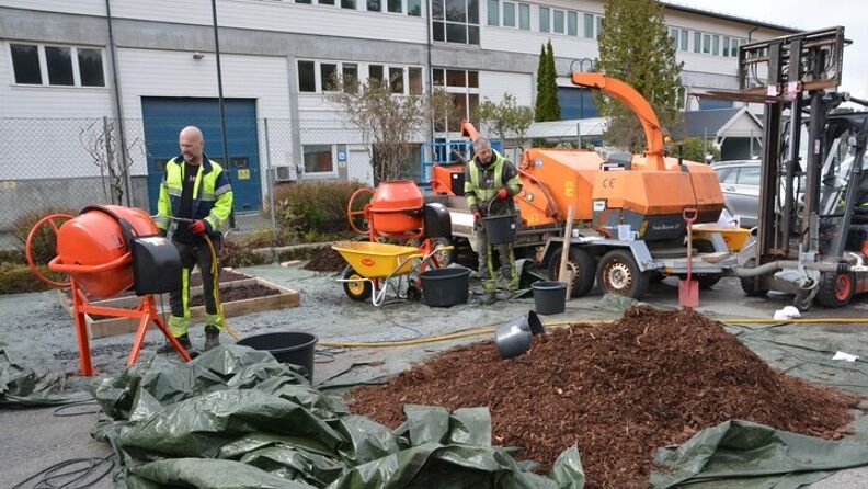 Foto av et to menn som jobber med betongblandere. En haug med brun bark er i forgrunnen av bildet. Fra prøvestøpet av LekeBARK. 
