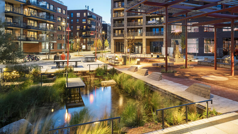 Vollebekk torg med vanndam, benker og lekestativ mellom leilighetsblokker.