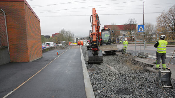 En gravemaskin og to arbeider som jobber med å byge holdeplass og sykkelvei.