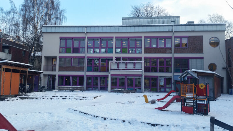 Lekeplass med barnehagen i bakgrunnen, to sklier med snø på bakken